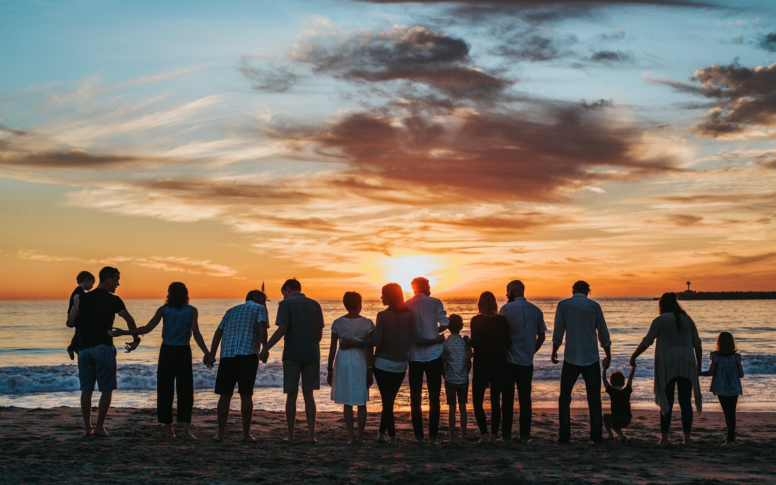 Die Familie steht Hand in Hand am Strand und schaut in den Sonnenuntergang